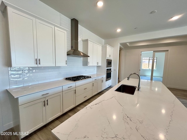 kitchen with tasteful backsplash, a sink, wall chimney range hood, dark wood-style floors, and stainless steel appliances