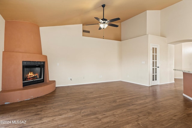 unfurnished living room with a towering ceiling, dark wood-type flooring, a large fireplace, and ceiling fan