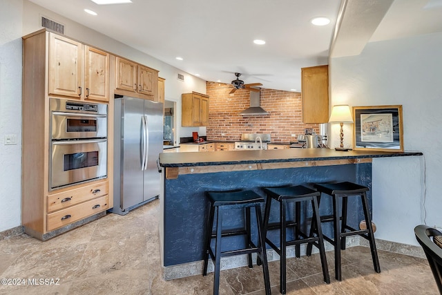 kitchen featuring kitchen peninsula, a kitchen bar, brick wall, stainless steel appliances, and ceiling fan