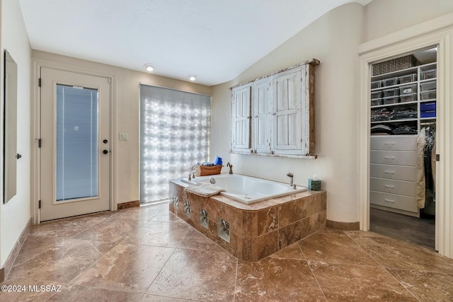 bathroom featuring a relaxing tiled tub and vaulted ceiling