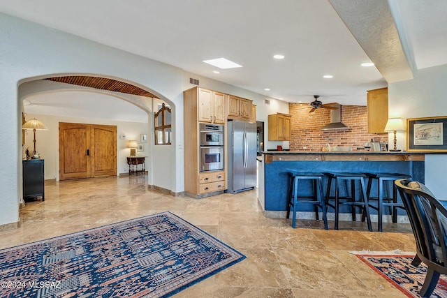 kitchen featuring a breakfast bar area, wall chimney exhaust hood, ceiling fan, kitchen peninsula, and stainless steel appliances