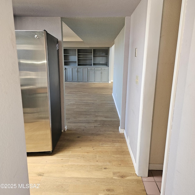 corridor with a textured ceiling and light hardwood / wood-style flooring