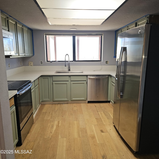 kitchen with appliances with stainless steel finishes, sink, green cabinets, and light wood-type flooring