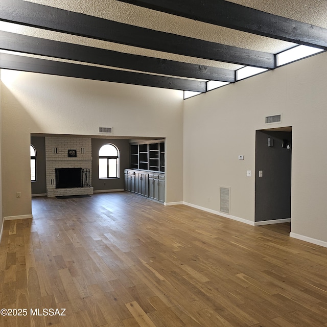 unfurnished living room featuring hardwood / wood-style flooring, a brick fireplace, a textured ceiling, and beam ceiling