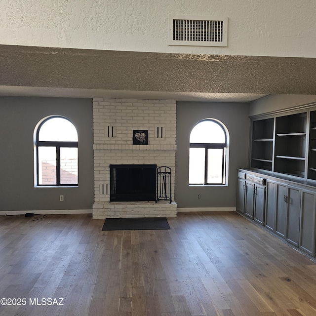 unfurnished living room featuring hardwood / wood-style flooring, a fireplace, a textured ceiling, and plenty of natural light