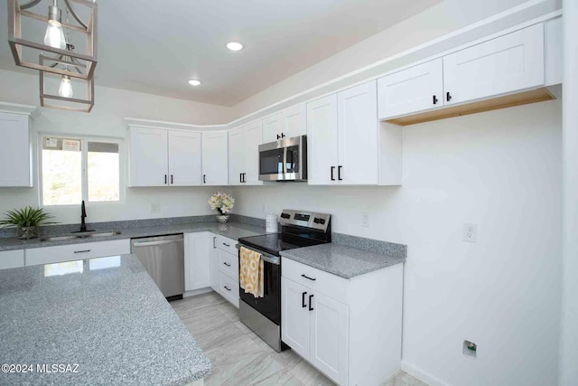 kitchen featuring appliances with stainless steel finishes, dark stone counters, sink, decorative light fixtures, and white cabinetry