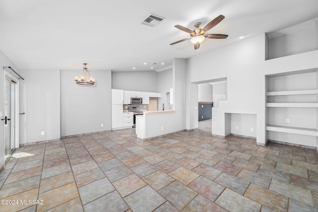 unfurnished living room with built in shelves, a towering ceiling, and ceiling fan with notable chandelier