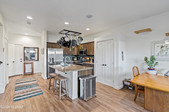 kitchen featuring appliances with stainless steel finishes, light wood-type flooring, a center island with sink, and light stone counters