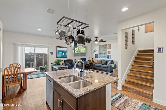 kitchen featuring sink, a center island with sink, stainless steel dishwasher, light hardwood / wood-style floors, and dark brown cabinetry