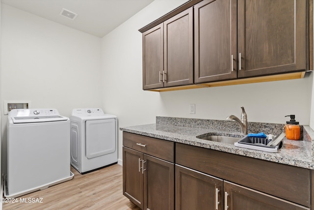 washroom with light hardwood / wood-style flooring, sink, washing machine and dryer, and cabinets