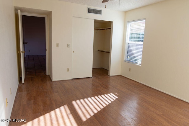 unfurnished bedroom featuring ceiling fan, hardwood / wood-style floors, a textured ceiling, a walk in closet, and a closet