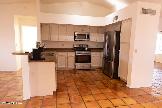 kitchen with sink, vaulted ceiling, light tile patterned floors, appliances with stainless steel finishes, and kitchen peninsula