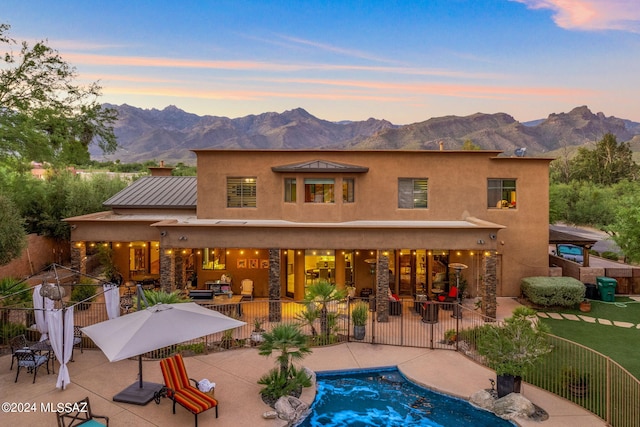 back house at dusk featuring a mountain view, a patio, and a fenced in pool