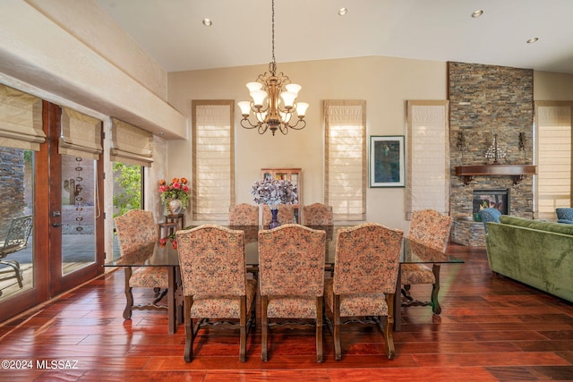 dining area with a chandelier, dark hardwood / wood-style flooring, a stone fireplace, and lofted ceiling