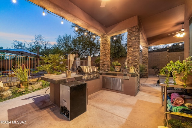 patio terrace at dusk with ceiling fan, grilling area, and exterior kitchen