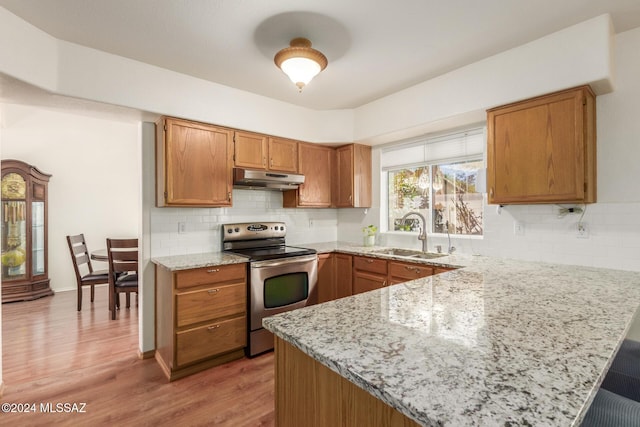 kitchen with stainless steel electric stove, sink, light wood-type flooring, light stone counters, and kitchen peninsula