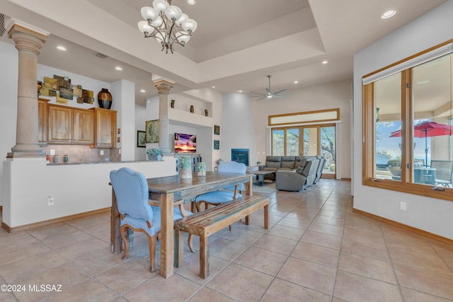 dining space with decorative columns, ceiling fan with notable chandelier, a large fireplace, a raised ceiling, and light tile patterned floors