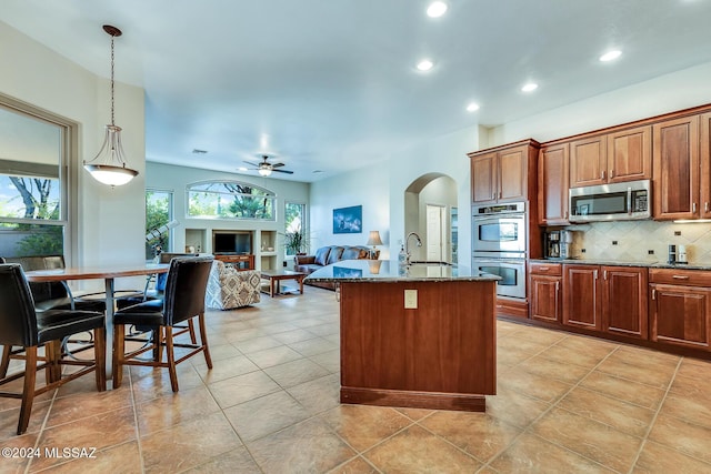 kitchen featuring ceiling fan, an island with sink, decorative light fixtures, decorative backsplash, and appliances with stainless steel finishes