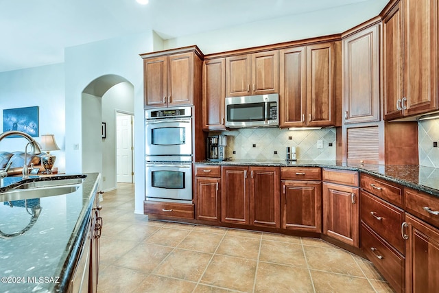 kitchen with backsplash, stainless steel appliances, sink, light tile patterned floors, and dark stone countertops