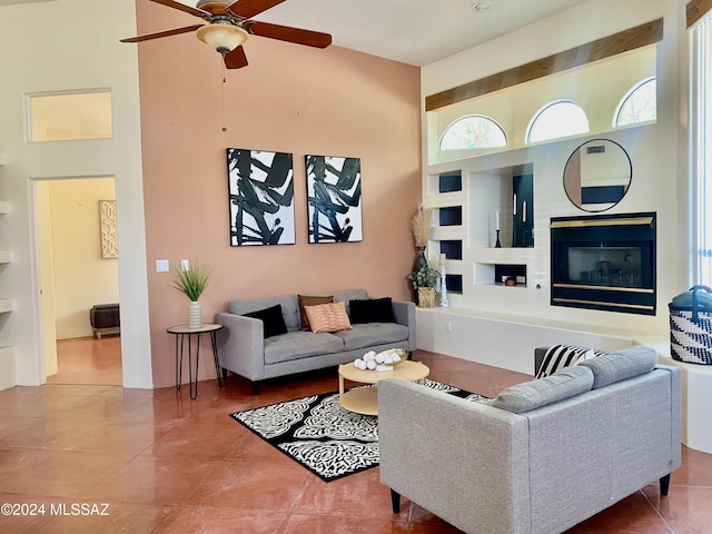 living room with built in shelves, ceiling fan, tile patterned flooring, and a towering ceiling