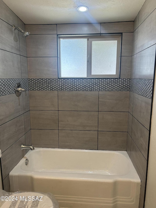 bathroom featuring toilet, a textured ceiling, and tiled shower / bath