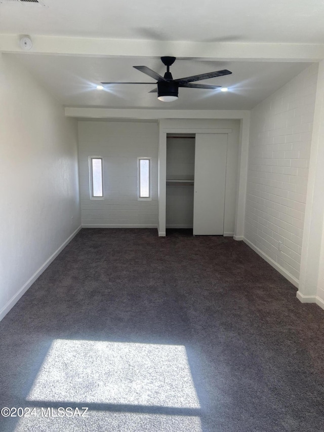 unfurnished bedroom featuring dark colored carpet, ceiling fan, and brick wall