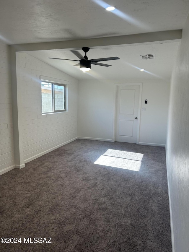 unfurnished room featuring lofted ceiling with beams, dark carpet, ceiling fan, and brick wall