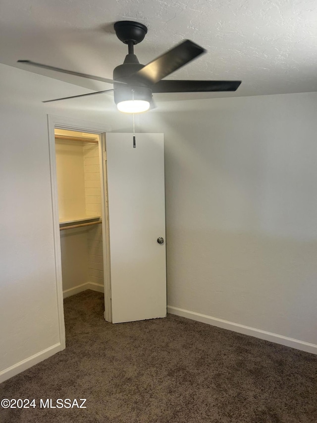 unfurnished bedroom featuring dark carpet, a walk in closet, ceiling fan, a textured ceiling, and a closet