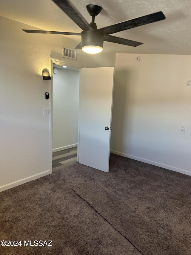 spare room with ceiling fan, dark carpet, and a textured ceiling