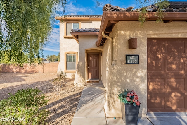 doorway to property with stucco siding, a tile roof, and fence