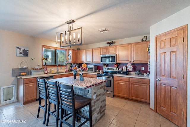 kitchen with light tile patterned floors, decorative light fixtures, a kitchen island, stainless steel appliances, and a chandelier