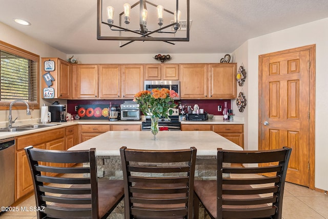 kitchen featuring stainless steel appliances, a sink, light tile patterned floors, light countertops, and a chandelier