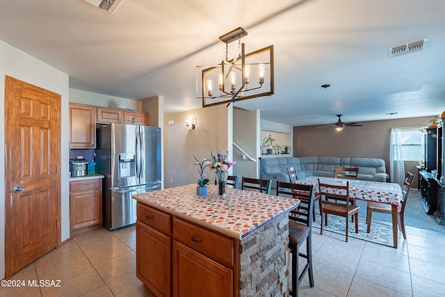 kitchen with pendant lighting, a center island, stainless steel fridge, light tile patterned flooring, and a kitchen bar