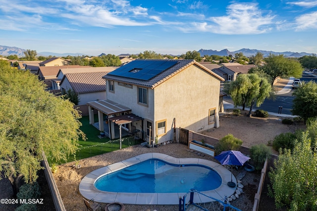 rear view of property featuring solar panels, a mountain view, an outdoor pool, stucco siding, and a fenced backyard