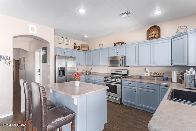 kitchen with a center island, blue cabinets, dark hardwood / wood-style floors, appliances with stainless steel finishes, and a breakfast bar area