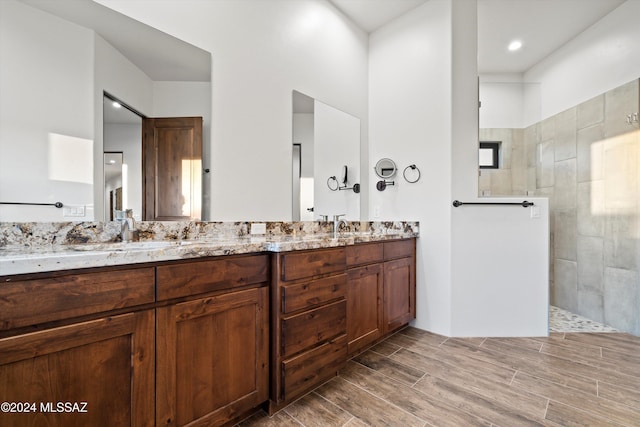 bathroom featuring double vanity, wood finish floors, walk in shower, and a sink
