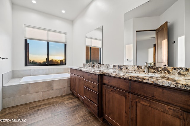 full bath with a bath, double vanity, wood finish floors, and a sink