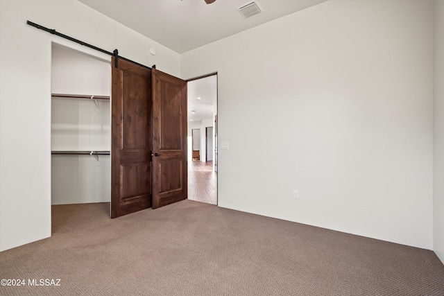unfurnished bedroom featuring visible vents, a closet, light carpet, a walk in closet, and a barn door