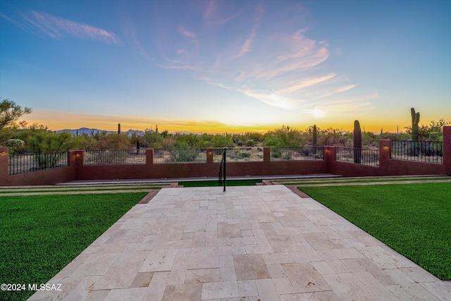 patio terrace at dusk featuring a lawn and fence