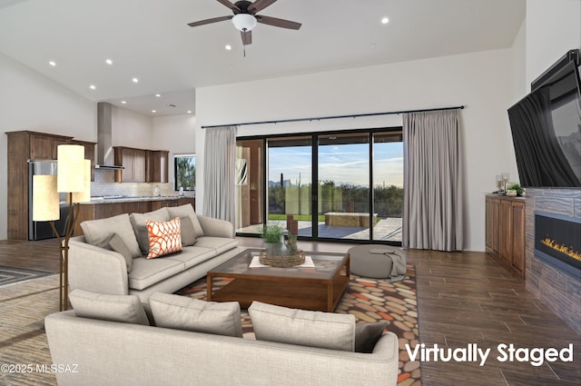 living area featuring ceiling fan, a glass covered fireplace, dark wood-style floors, recessed lighting, and a towering ceiling