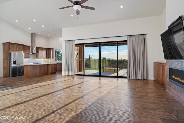 unfurnished living room with dark wood-type flooring, recessed lighting, a high ceiling, a glass covered fireplace, and a ceiling fan