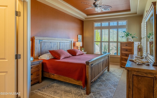 carpeted bedroom with a raised ceiling and ceiling fan