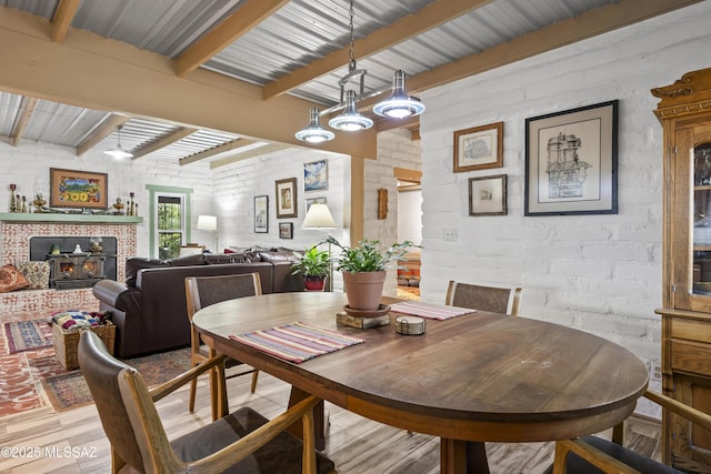dining room with light hardwood / wood-style flooring, beamed ceiling, and brick wall