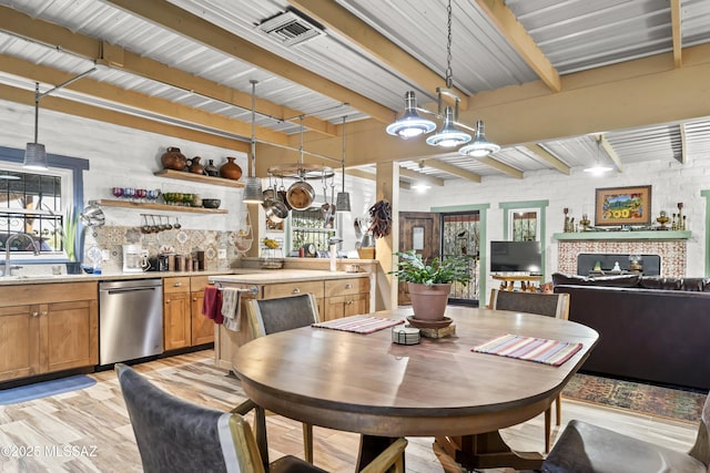 dining room featuring brick wall, sink, light hardwood / wood-style flooring, beamed ceiling, and plenty of natural light