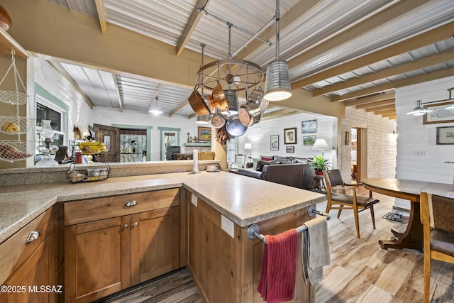 kitchen with beamed ceiling, light hardwood / wood-style floors, kitchen peninsula, and brick wall