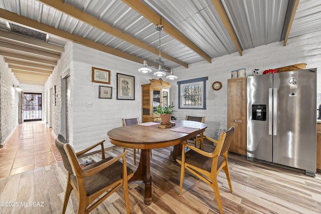 dining space with beam ceiling and brick wall
