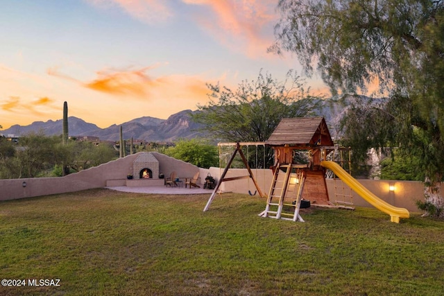 playground at dusk with a lawn, a mountain view, and an outdoor brick fireplace