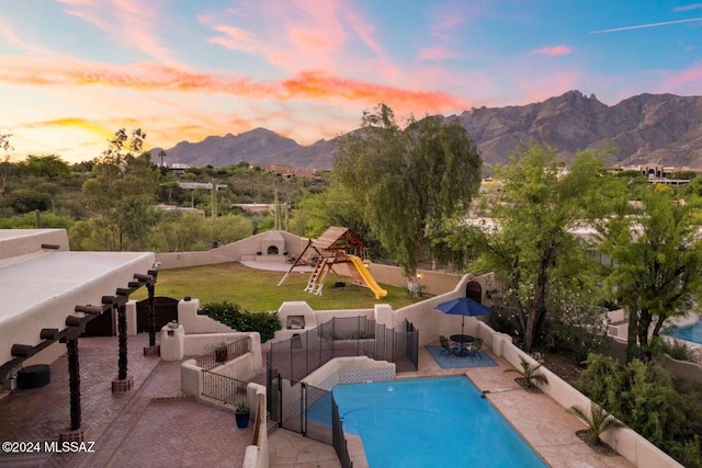 pool at dusk with a mountain view, a patio, and a playground