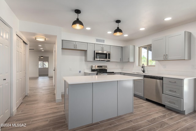 kitchen with stainless steel appliances, pendant lighting, hardwood / wood-style flooring, a center island, and gray cabinets