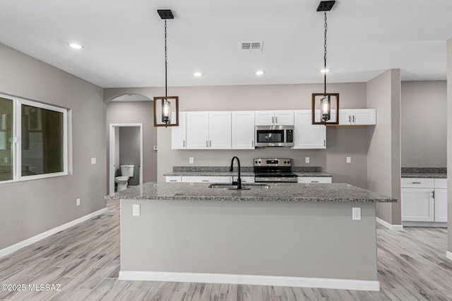 kitchen with light stone counters, white cabinetry, decorative light fixtures, a center island with sink, and appliances with stainless steel finishes